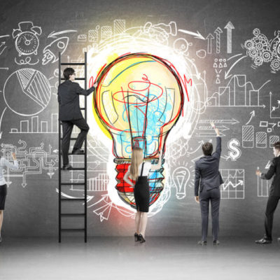 Rear view of business team near blackboard with colorful light bulb and startup sketch drawn on it. Concept of idea of business
